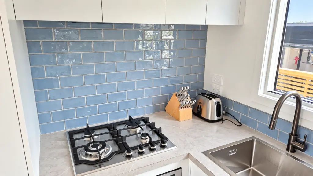 Tiny home kitchen with gas hob, blue-grey tiled splashback and stainless steel sink