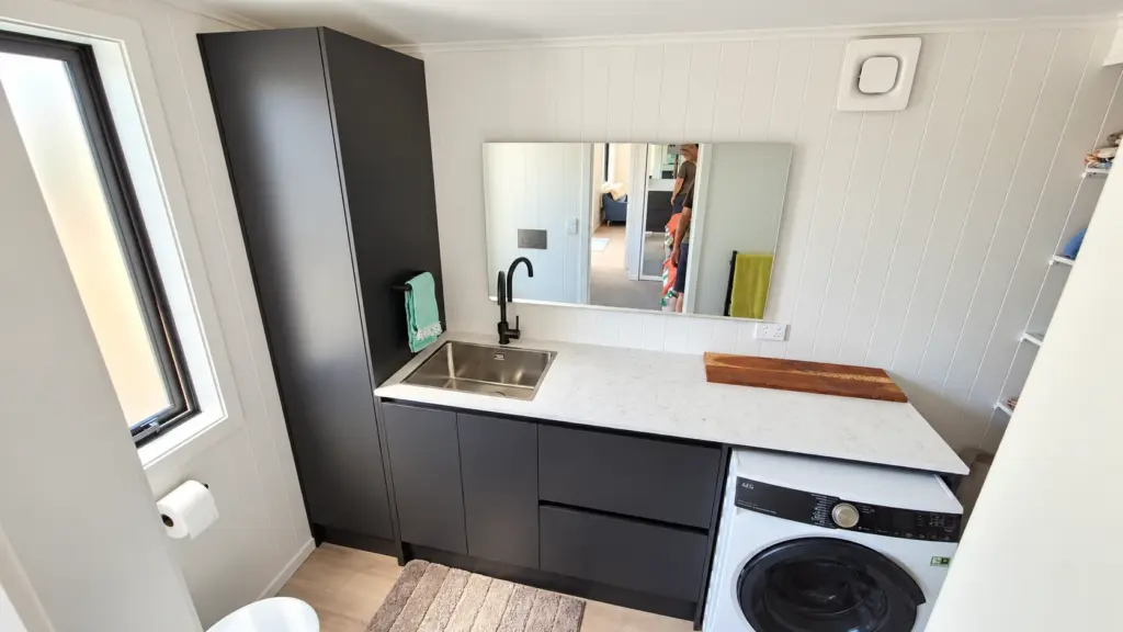 Tiny home laundry and bathroom with front-loading washing machine and dark cabinetry
